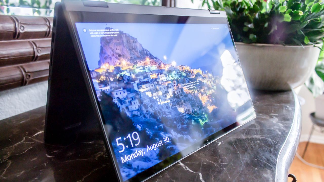 An open and powered on laptop stands on top of a black marble countertop with its keyboard folded behind the display