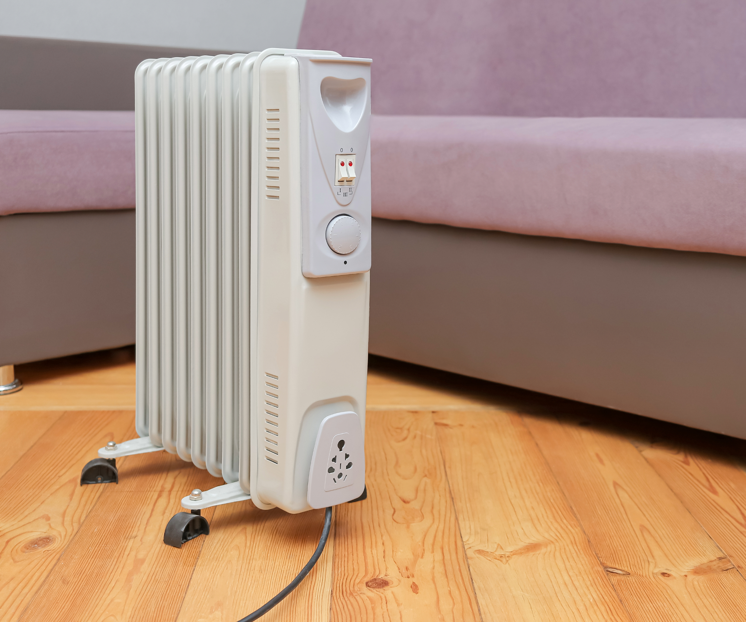 Oil filled radiator on a wooden floor in front of a purple sofa