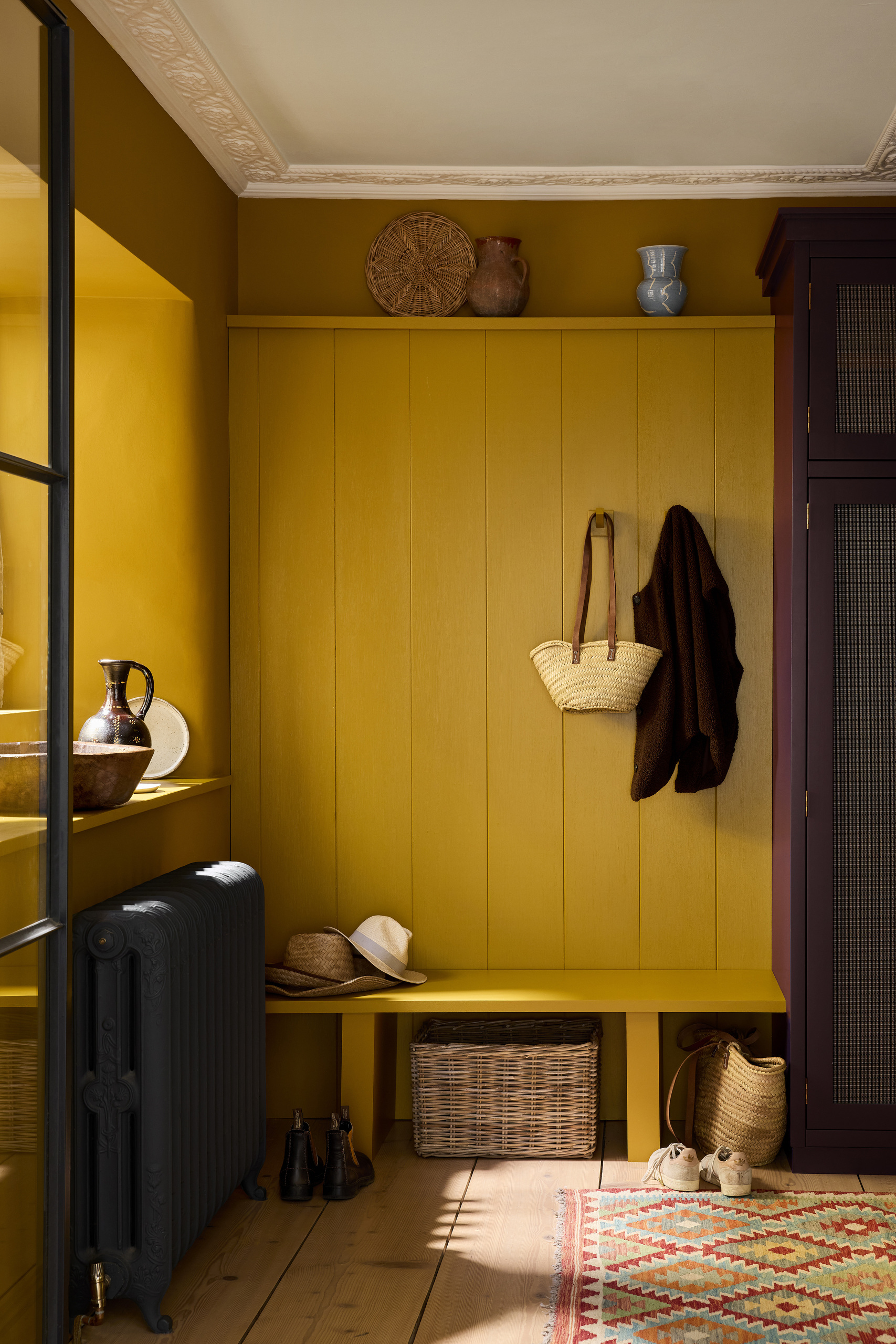 A cozy entryway painted in a bright sunflower yellow with a purple built-in cupboard to the left of the bench seat.