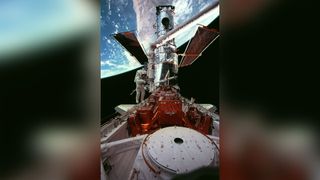 wide shot of the Hubble Space Telescope (HST) in Discovery's cargo bay, backdropped against Australia, with astronaut Steven L. Smith.