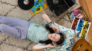 Best portable record players: Woman lying on a rug wearing headphones and surrounded by vinyl albums