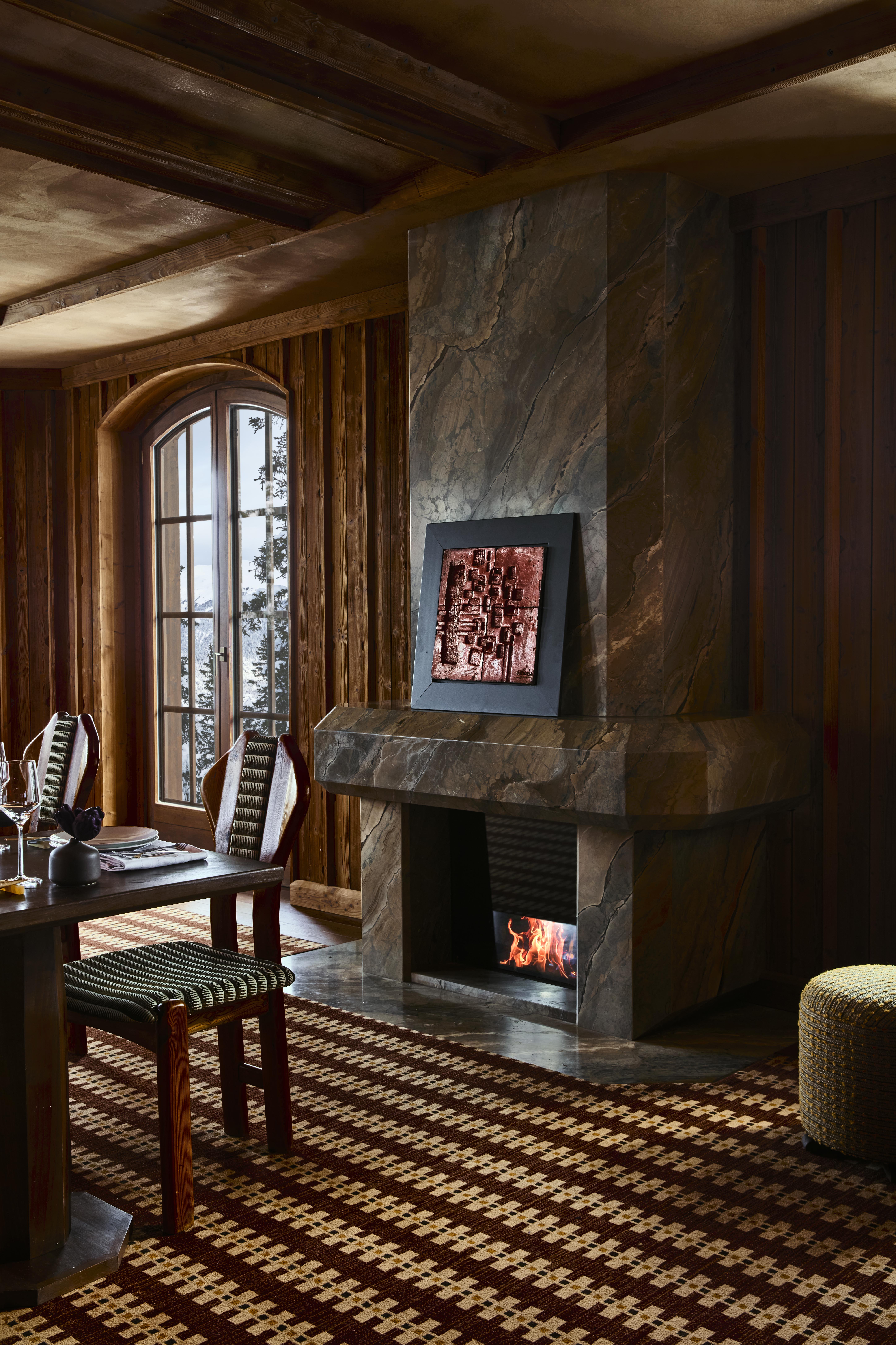 The elaborate, theatrical interiors of a ski chalet with wood wall paneling, plush textiles in different patternes, colors, and textures, plenty of paintings and sculptures adorning its halls, and a dimly lit atmosphere.