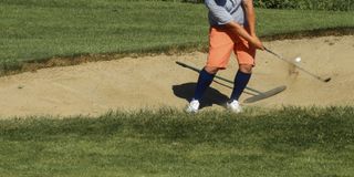 Golfer plays a bunker shot wearing long socks