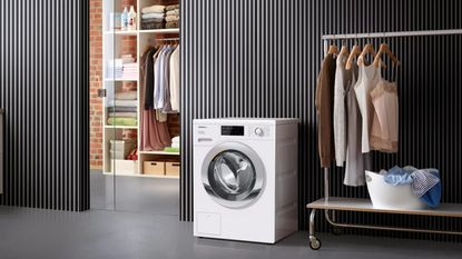 a Miele washing machine (the Miele WEG365 WCS Washing Machine) in a closet, with clean clothes hung up around it