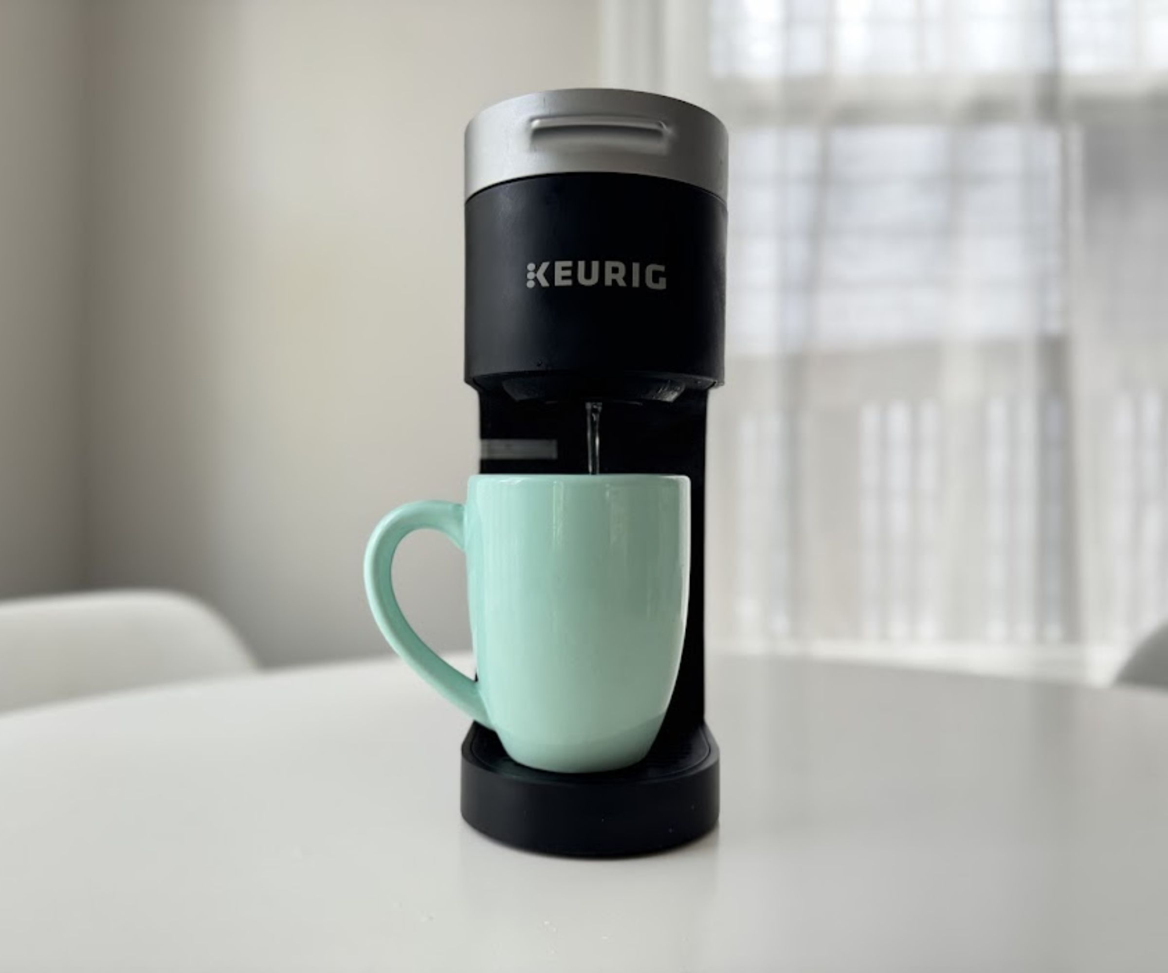 A black Keurig machine running a cycle, emptying clear water into a blue coffee mug.