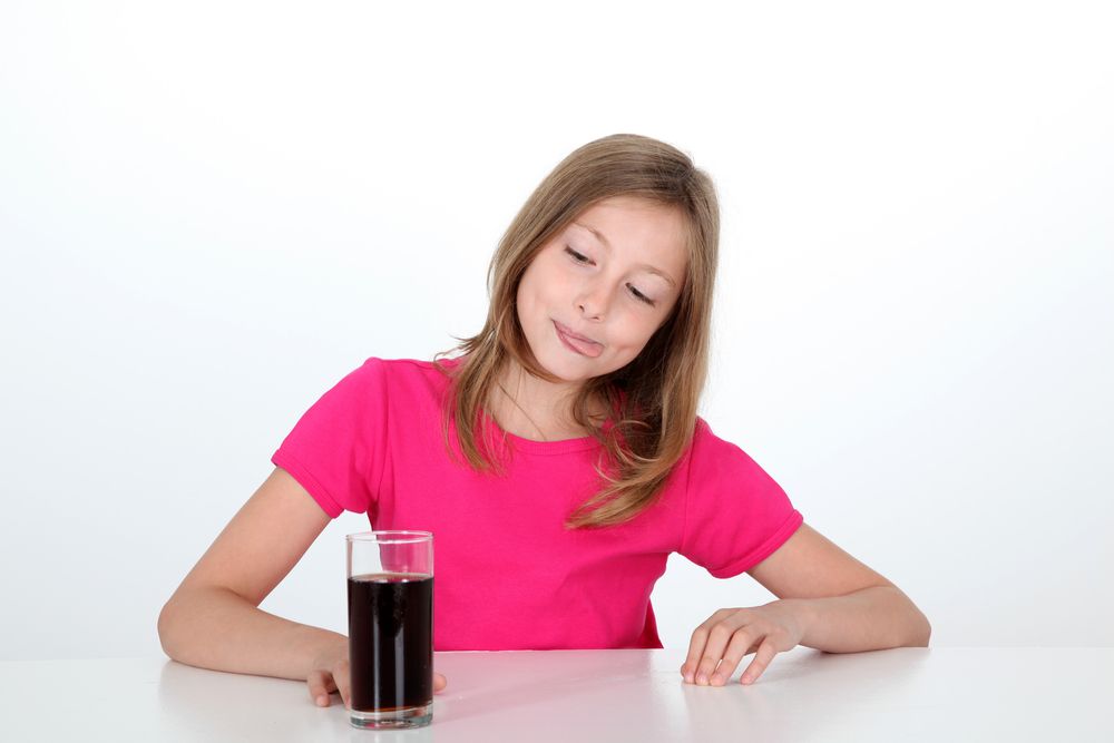 A girl sits looking at a glass of soda.