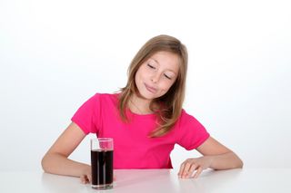 A girl sits looking at a glass of soda.