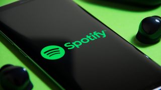 Die Spotify-App auf einem Smartphone, daneben ein Paar kabellose Ohrstöpsel