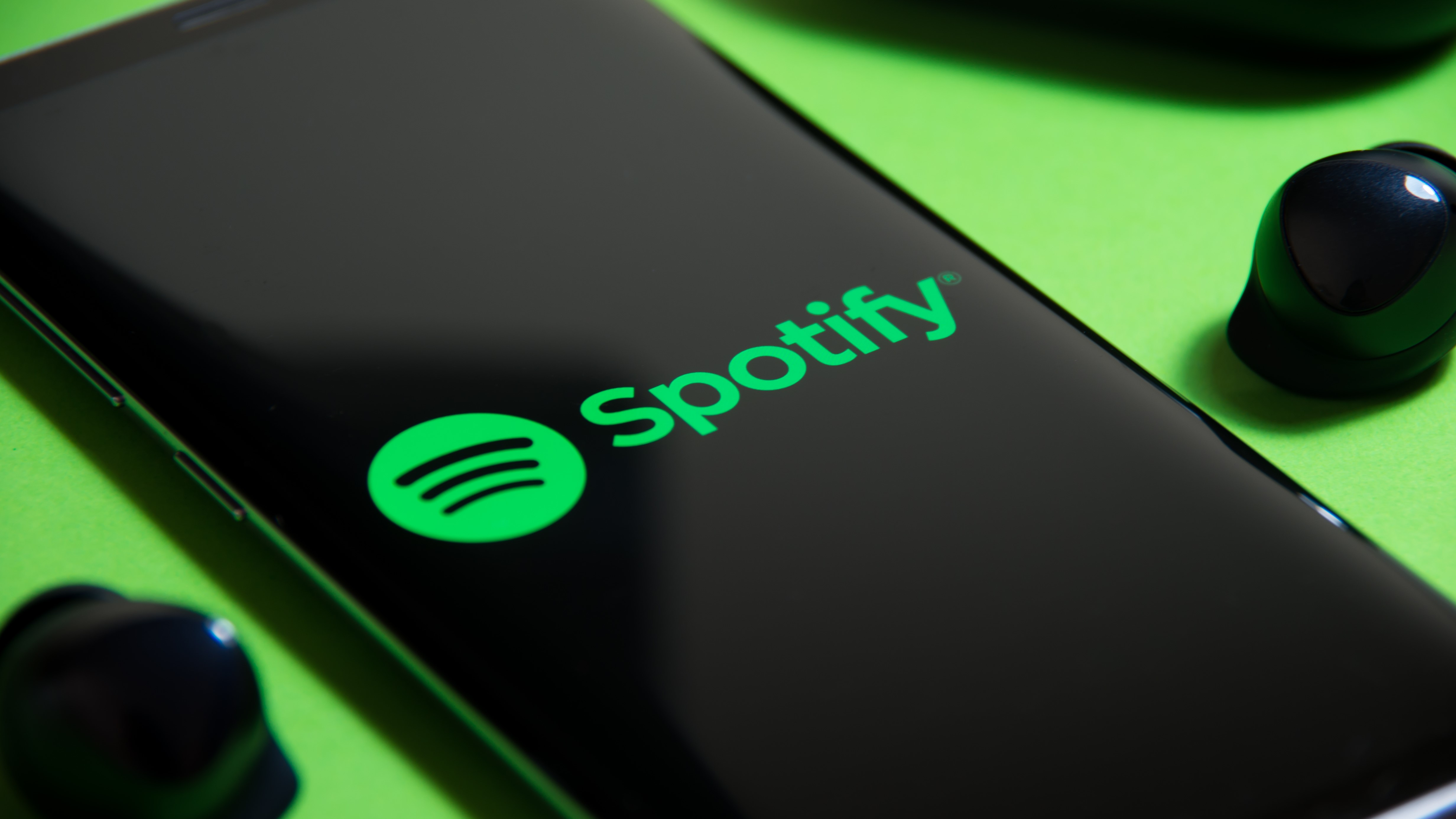 برنامه Spotify در تلفن هوشمند در کنار یک جفت هدفون بی سیم واقعی