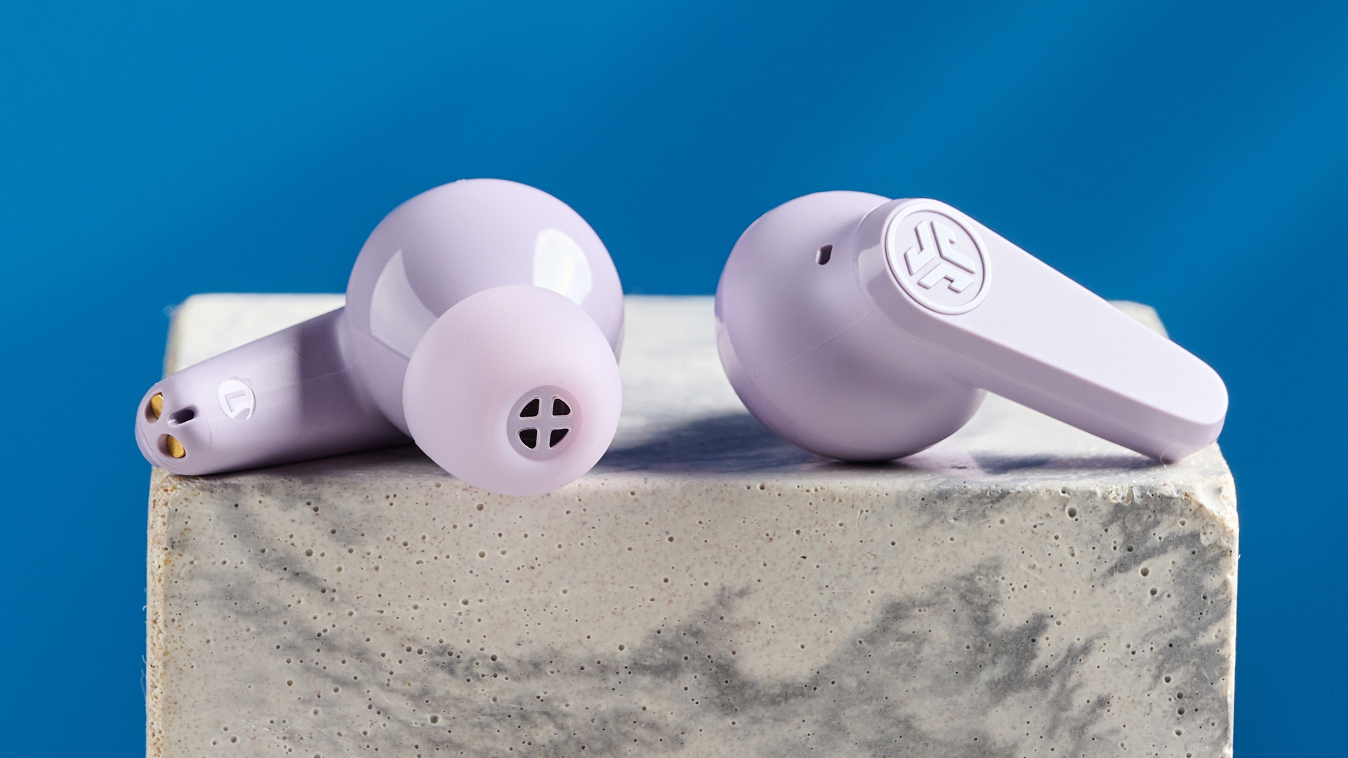 the jlab go pods anc earbuds in lilac with a lilac charging case and built in usb-c cable against a blue background on a marble stand