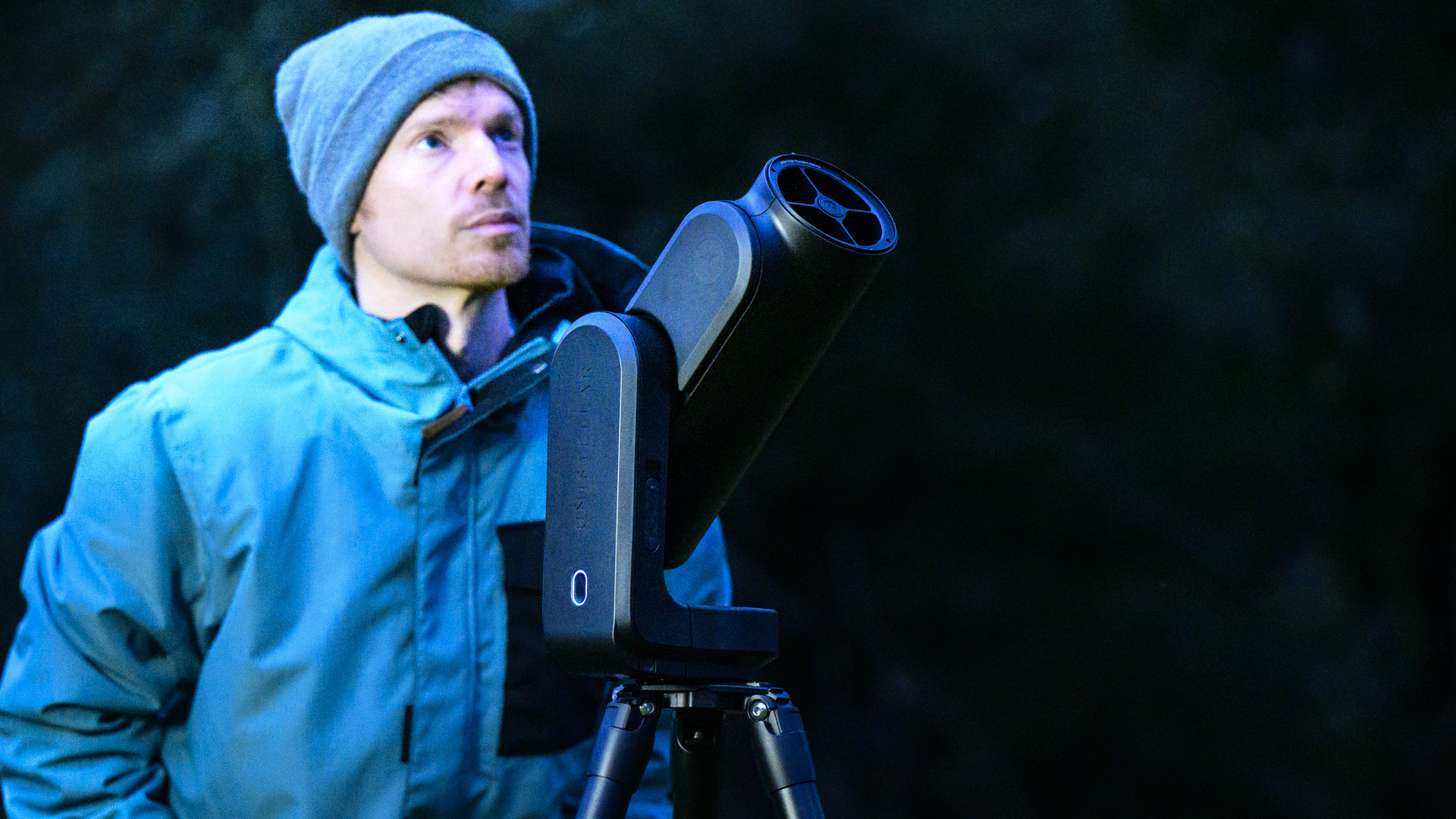 Person looking up into the night sky alongside the Unistellar Odyssey Pro telescope