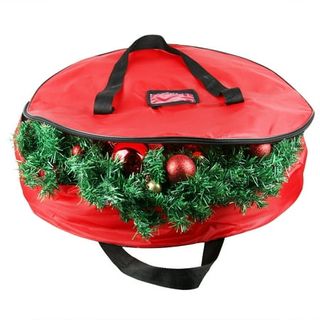 A round red fabric storage bag with long black handles, unzipped to show half of a green Christmas wreath