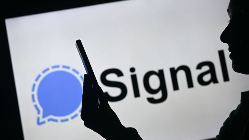 A woman holding a mobile phone in front of the Signal logo displayed on a computer screen