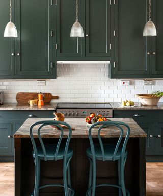 Dark green kitchen with kitchen island, green bar chairs and pendant lights