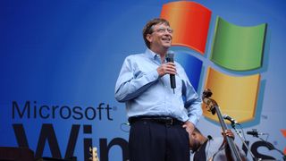 Bill Gates se tient sur la scène avec le logo Windows XP derrière lui.