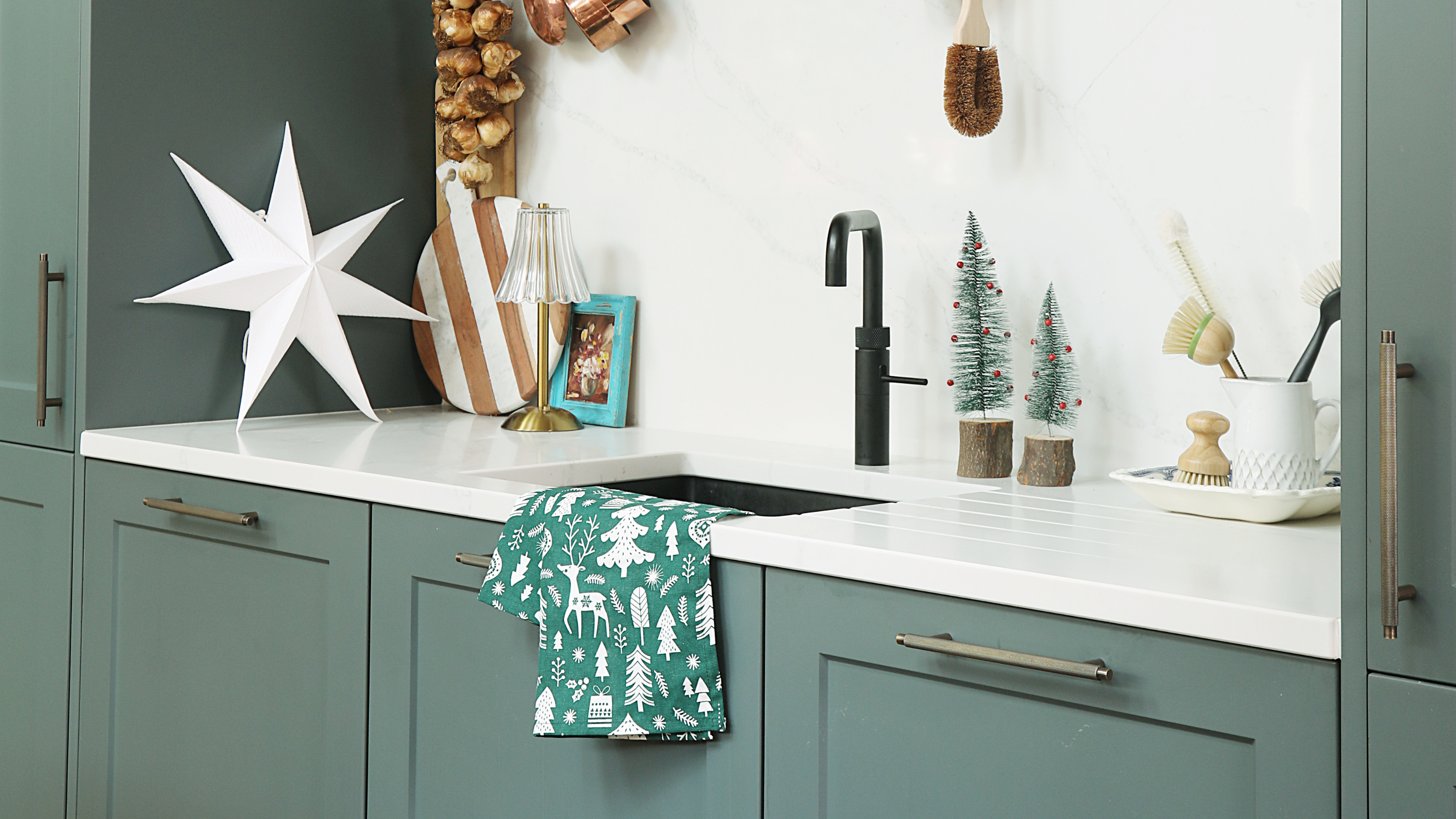 Green kitchen with Christmas decorations. There is a green Chirstmas-themed tea towel on the sink.