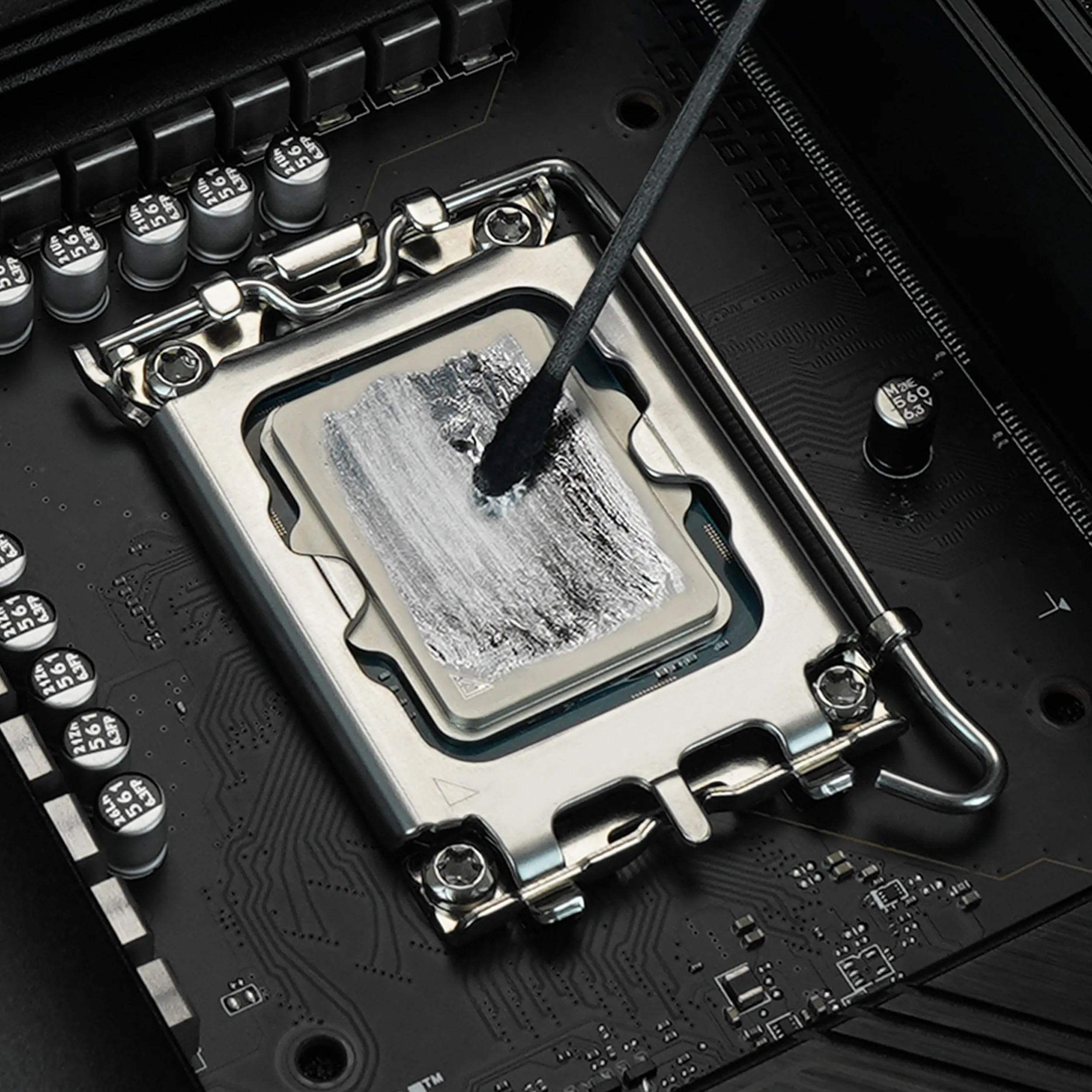 A brush spreads silver liquid metal across the heat spreader of a CPU in a motherboard socket