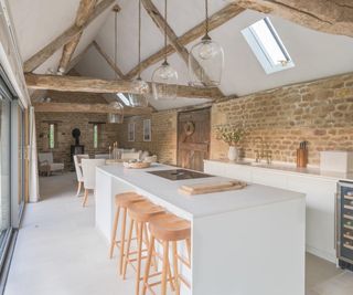 interior of barn conversion with exposed beams, trusses, stone walls and a modern white kitchen