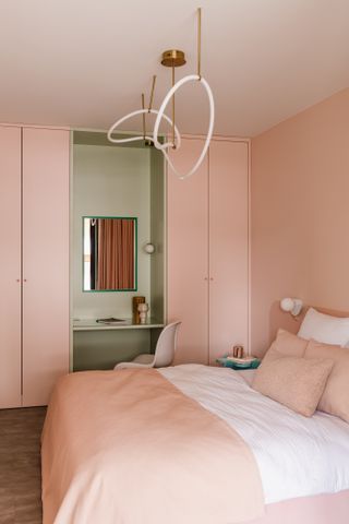 A bedroom with light pink interiors and a green small cabinet