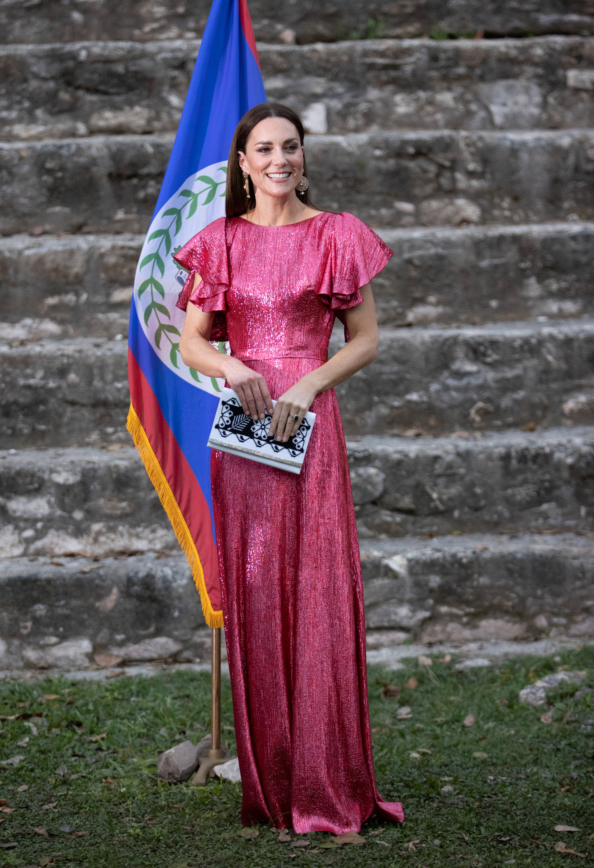 Kate Middleton wearing a pink sequined gown standing in front of a flag in the grass