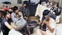 Beatle George Harrison receiving instruction in playing the sitar from a Sikh teacher as the other members of the Beatles look on in quiet fascination, July 1966