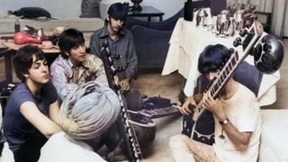 Beatle George Harrison receiving instruction in playing the sitar from a Sikh teacher as the other members of the Beatles look on in quiet fascination, July 1966