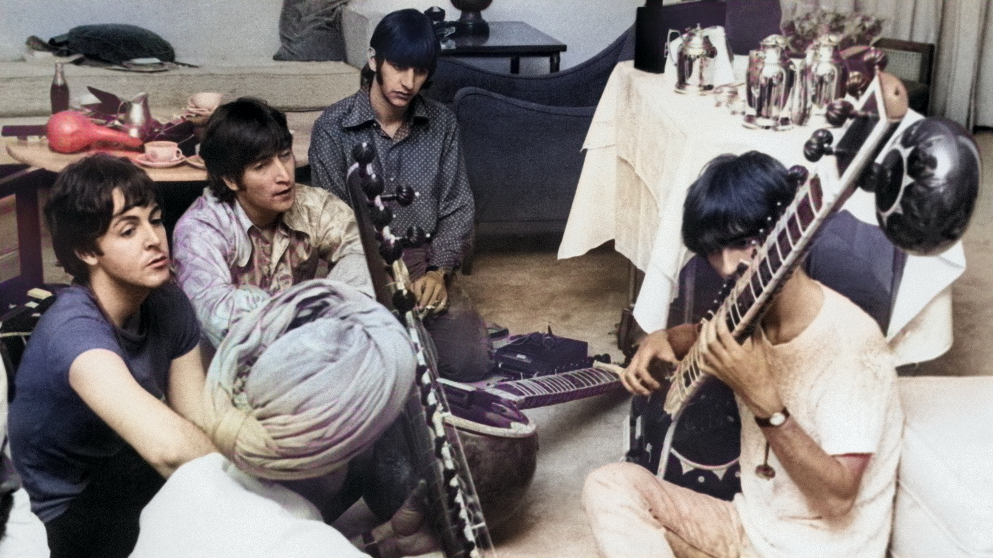 Beatle George Harrison receiving instruction in playing the sitar from a Sikh teacher as the other members of the Beatles look on in quiet fascination, July 1966