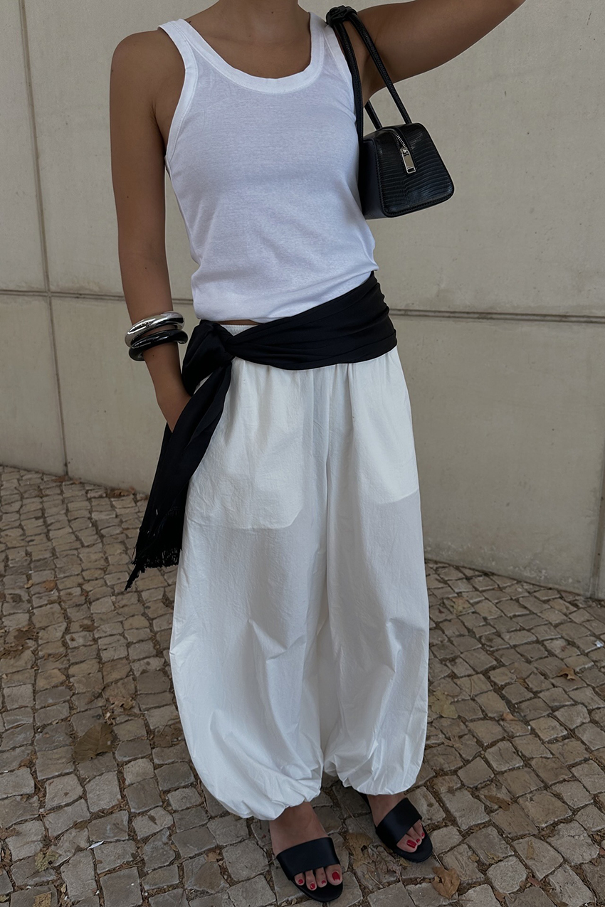 a woman wearing a white tank, white pants, and black scarf on her waist