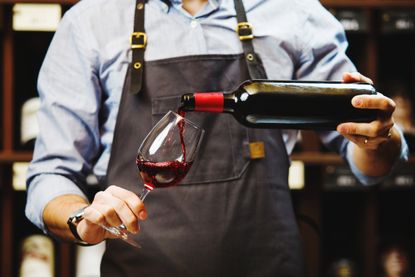 Male sommelier pouring red wine.
