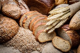 An image of a bunch of whole grains including bread and wheat stalks.