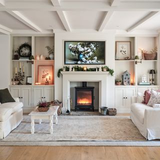 a cosy living room with a lite wood burning stove in the centre, alcove shelving and built-in cupboards either side of the chimney breast, and two matching cream sofas, facing inwards