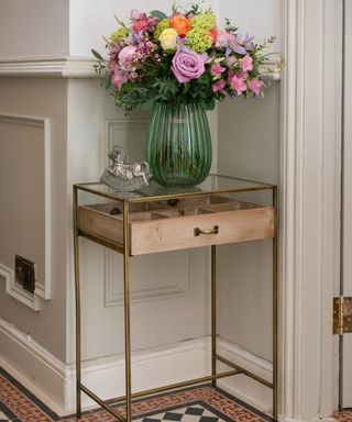 A small entryway corner with a colorful bouquet of flowers on top of a gold console table