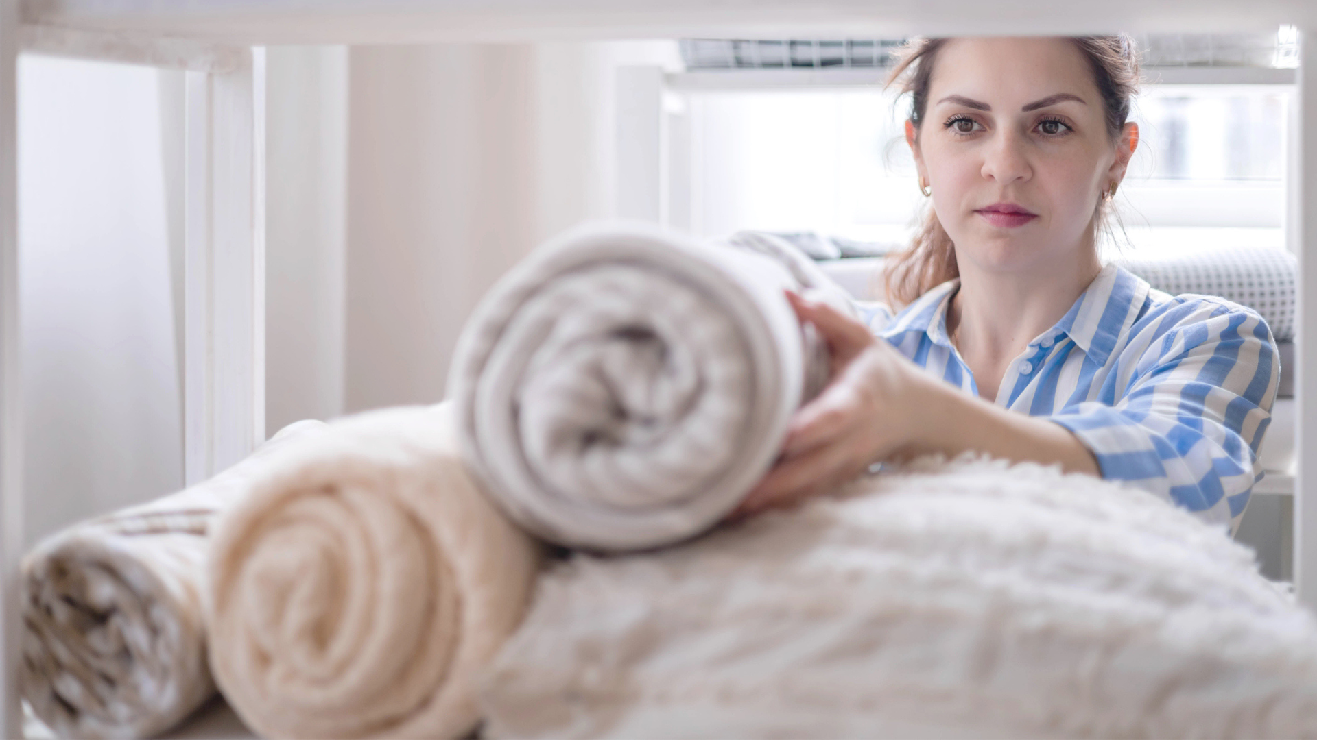Woman folding and rolling bedding to keep them organised in the cupboard
