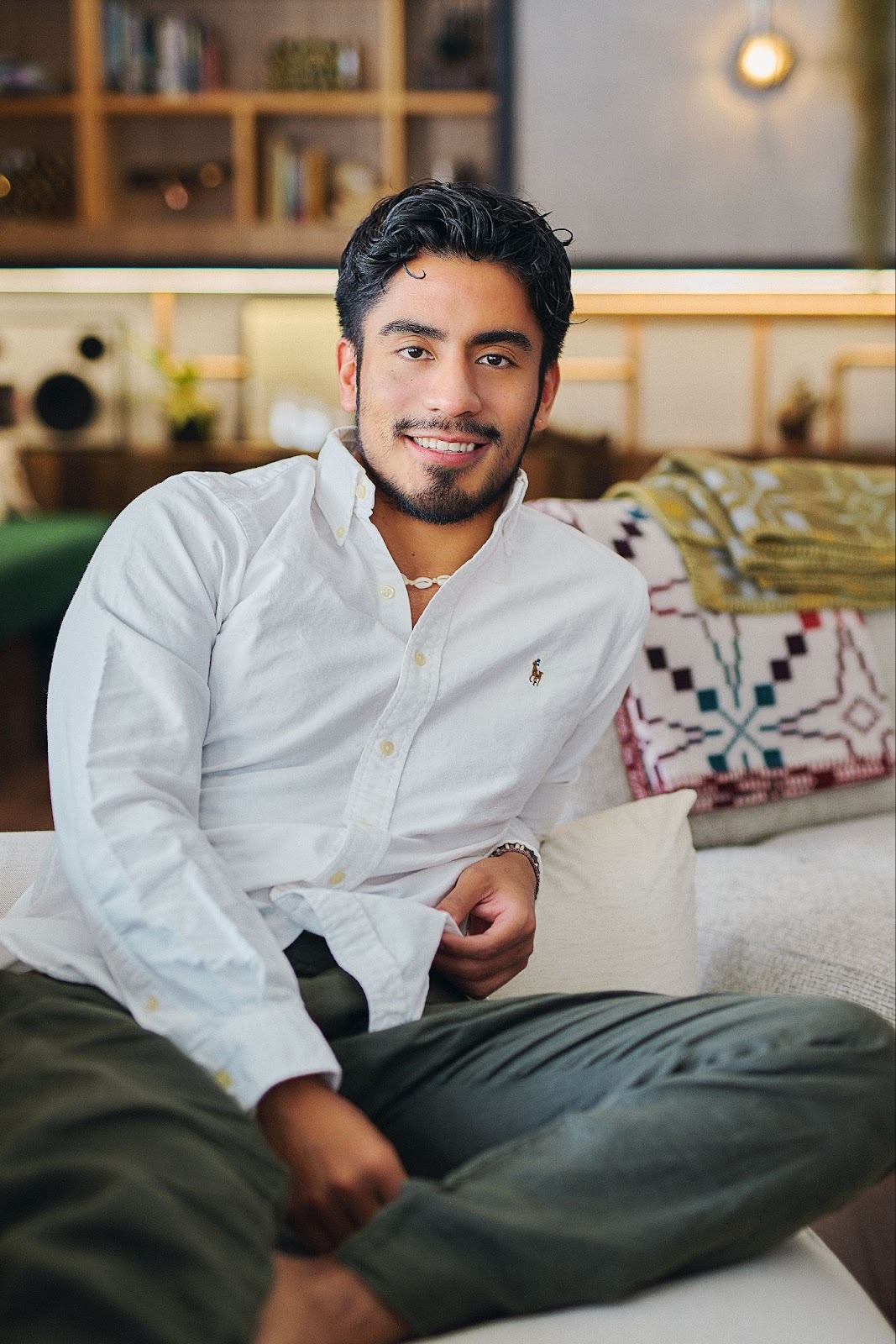A Peruvian man named William wears a white button-down and jeans while sitting on a sofa, in a cast portrait for 'The Boyfriend.'