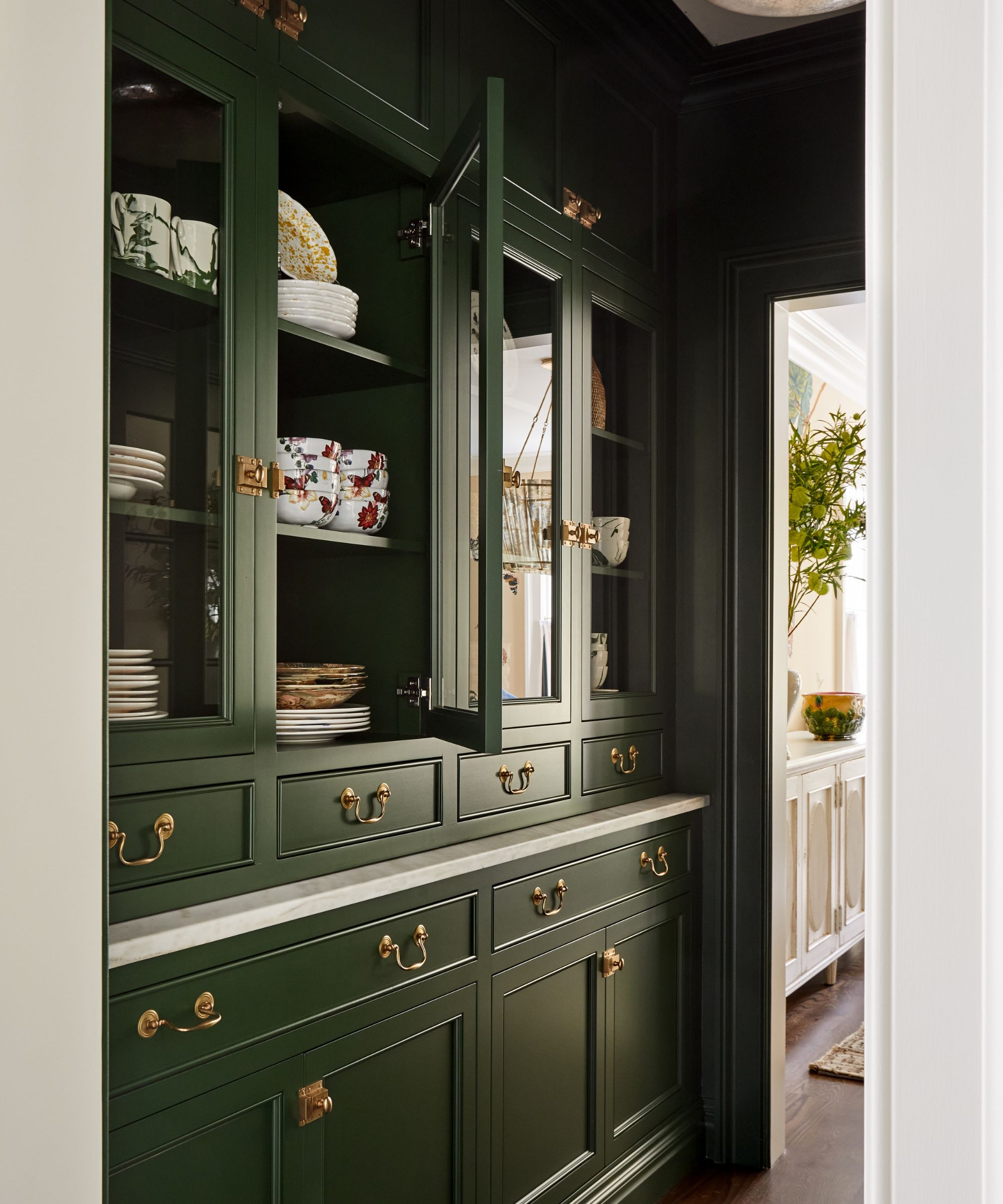 A butler's pantry with dark green cabinets with traditional brass hardware.
