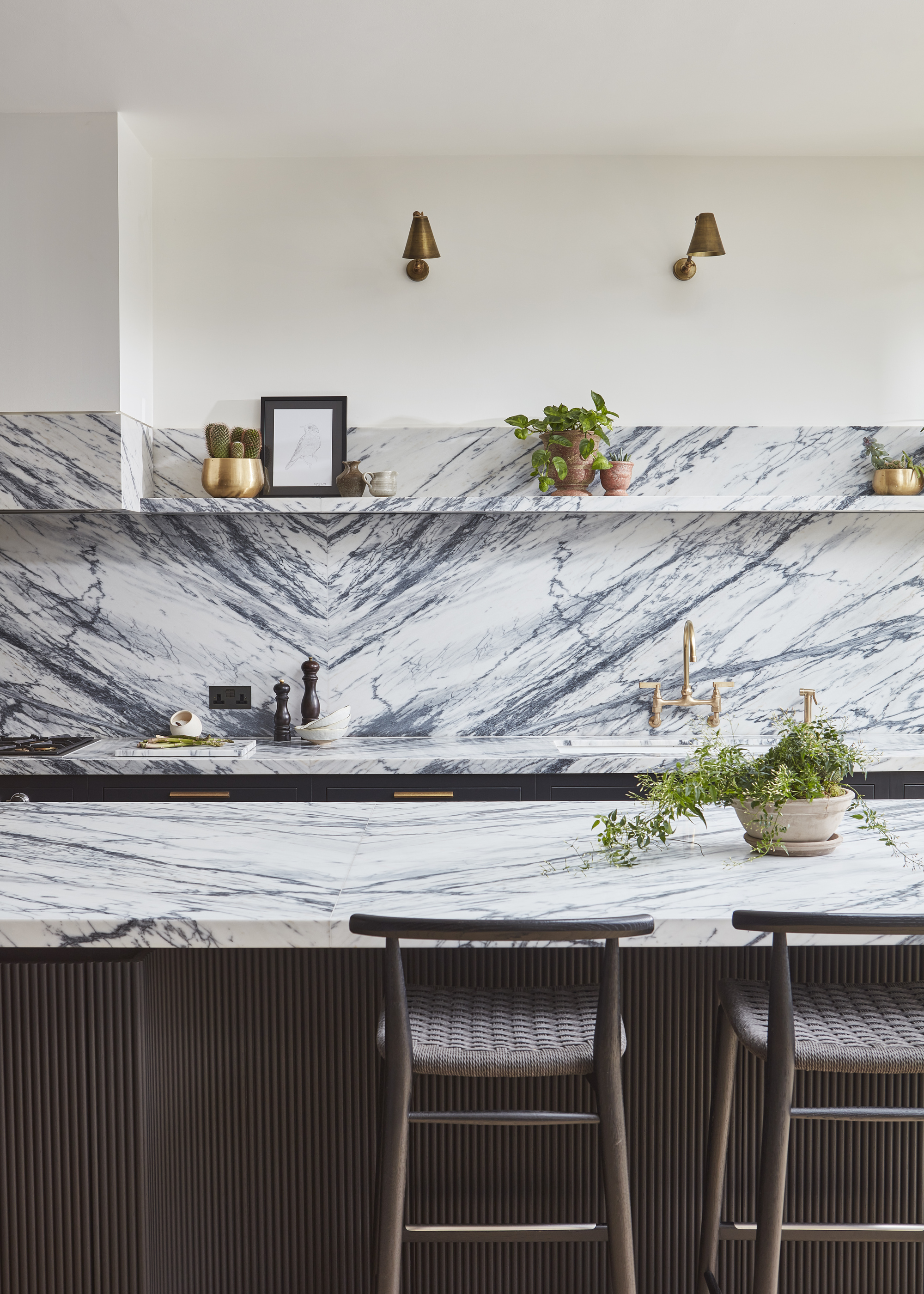 A minimalist kitchen with a bookmatched marble countertop and backsplash, an open shelf, and bar stools at the island