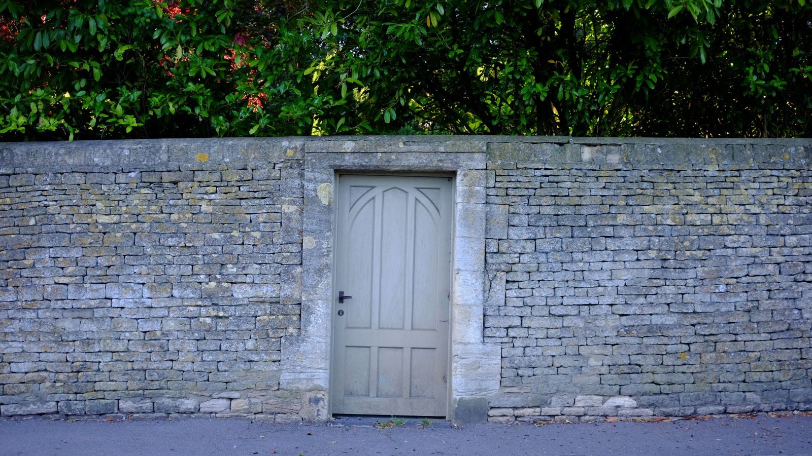 A grey wooden garden gate with a black handle surrounded by a grey brick garden wall