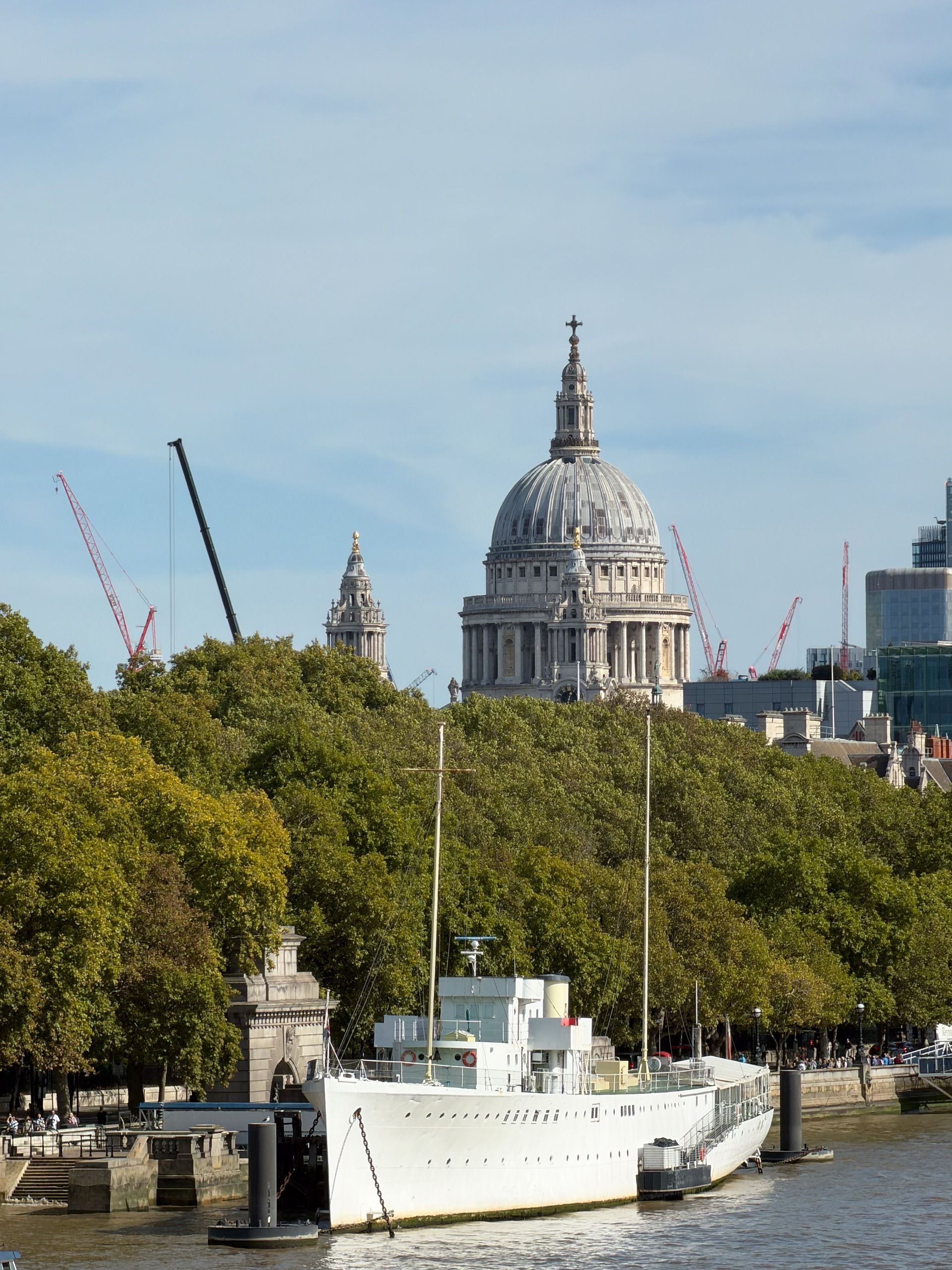 St Paul&rsquo;s Cathedral rising above trees and a moored white ship on the River Thames in London.