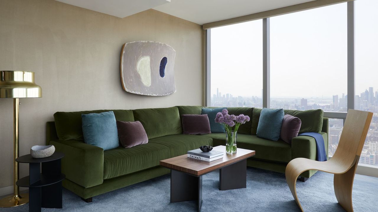 Green velvet sofa in the living room with blue and purple cushions, wood coffee table with flowers, gold floor lamp, and wood curved chair