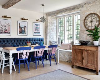 kitchen dining area with black banquette seating, blue and pink chairs and white wooden table in 12th century Cotswolds country house