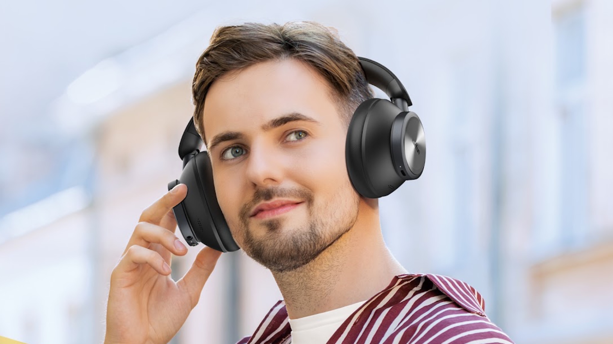 A man with dark hair and a goatee beard is listening to a pair of EarFun Wave Pro X headphones