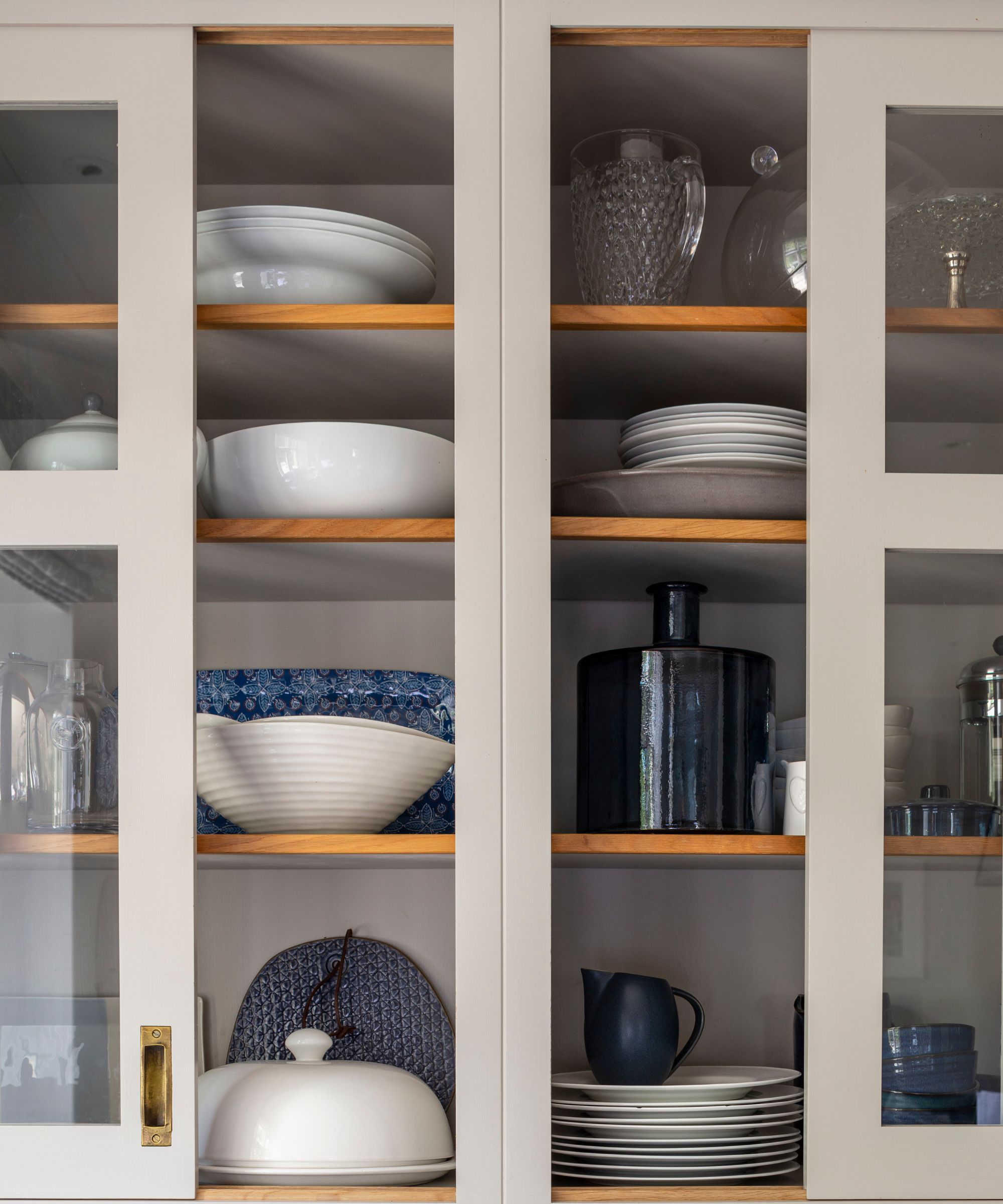 Glass front kitchen cabinets with stacks of white plates, bowls, glassware and jugs.