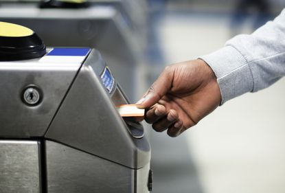Man inserting train ticket into train station barrier