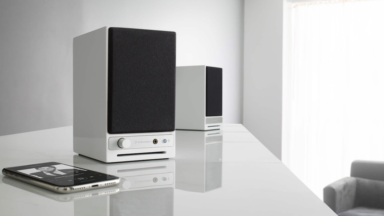 Audioengine HD3 Next-Gen (2025) in white on a white background in a white room. There's a black phone next to the speakers.