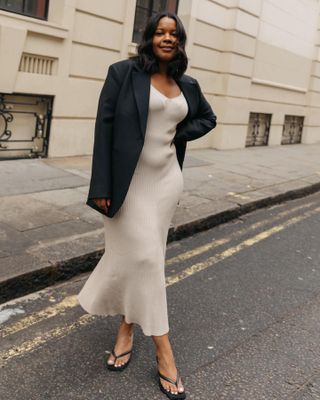 Fashion influencer Karina from Style Idealist poses on the streets of New York City in a black blazer, beige ribbed sweater dress and black flip-flop kitten heels