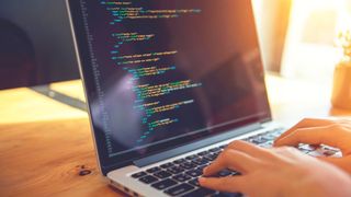 An unidentified person coding on a laptop placed on a bright desk