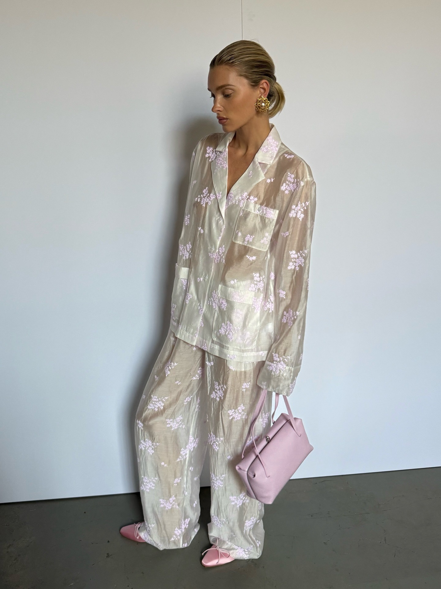 Elsa Hosk wears a white matching pant set with baby pink flats and a pink bag.