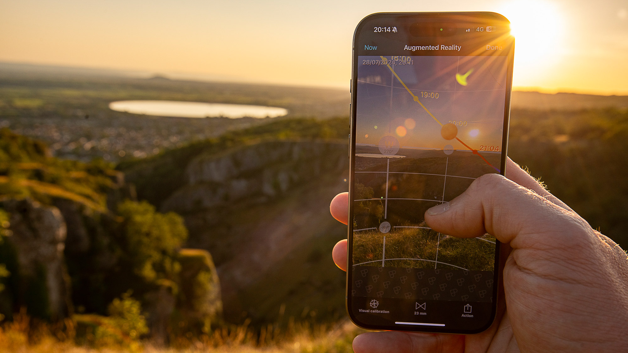 A person holding a smartphone at sunset using the PhotoPills app augmented reality to find out where the sun will set on the horizon