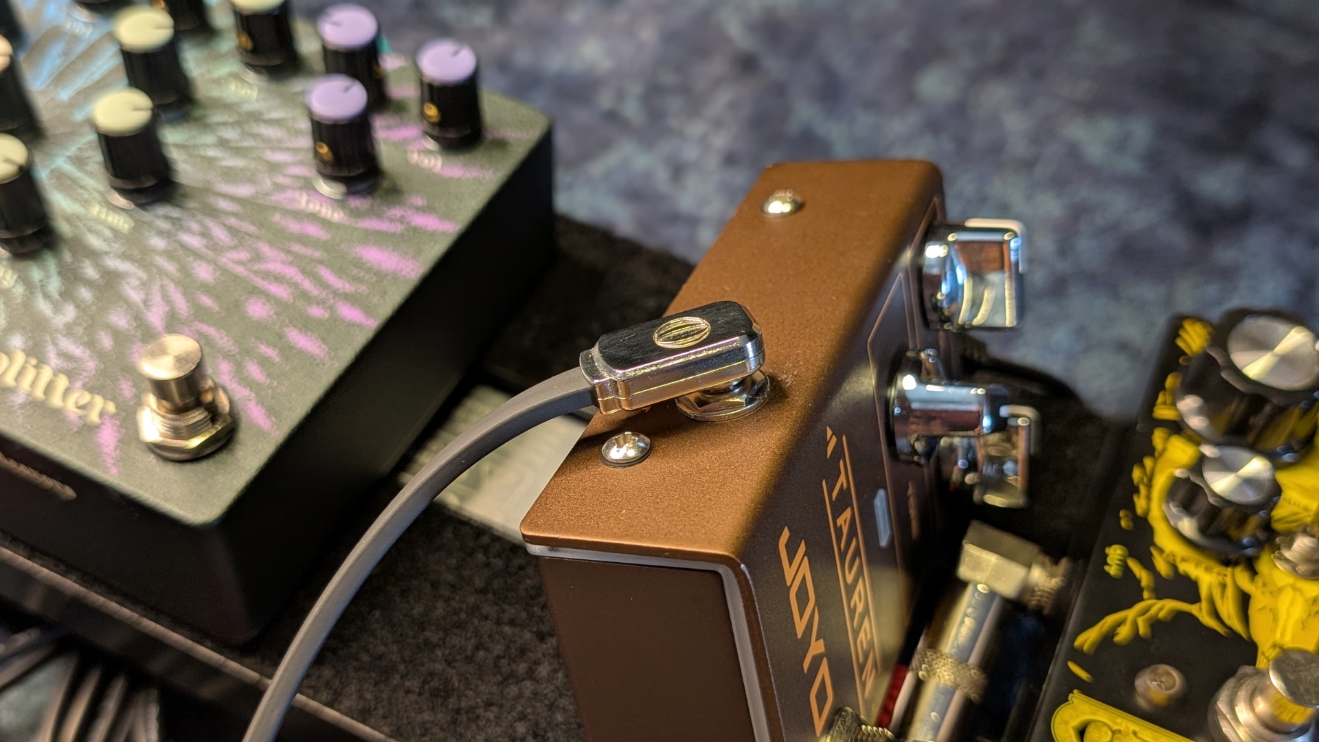 A patch cable plugged into an overdrive pedal on a pedalboard