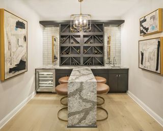 Bar with stools either side in room with built-in wine fridge, storage, sink and wine rack above